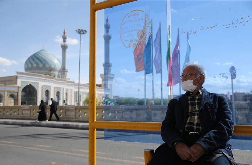 A man wearing a protective face mask, following the outbreak of coronavirus disease (COVID-19), sits at a bus stop in Qom, Iran March 24, 2020 (photo credit: REUTERS)