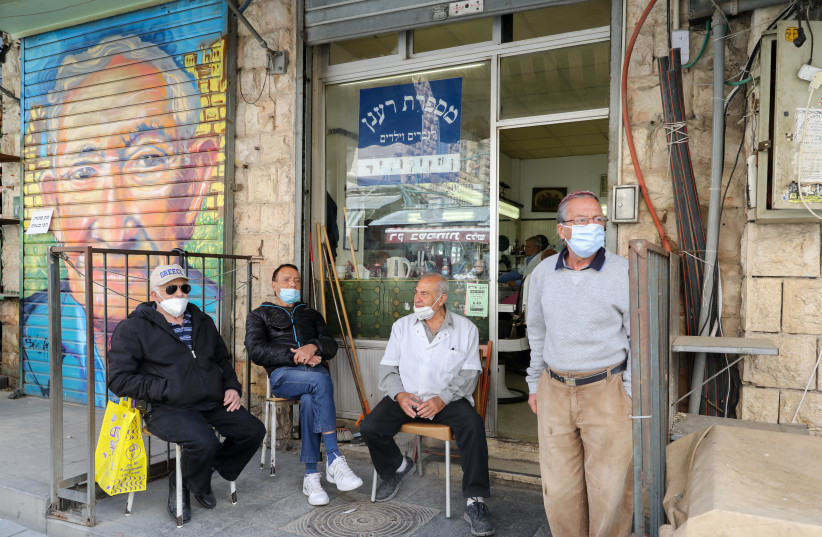People sitting outside a barber shop at Jerusalem's Mahane Yehuda amid coronavirus restrictions (photo credit: MARC ISRAEL SELLEM/THE JERUSALEM POST)