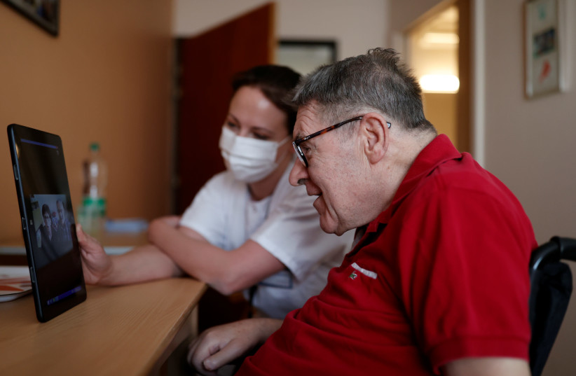 Health worker Emilie Neumann helps a 79 year-old resident to attend an online video call with his relatives at Les Jardins d'Emeraude long-term care unit at Bischwiller departemental hospital, near Strasbourg, during a lockdown imposed to slow the spread of the coronavirus disease (COVID-19), France (photo credit: REUTERS/CHRISTIAN HARTMANN)