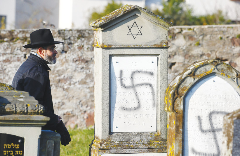A MAN WALKS past graves desecrated with swastikas at the Jewish cemetery in Westhoffen, near Strasbourg, France, in December 2019. (photo credit: ARND WIEGMANN / REUTERS)