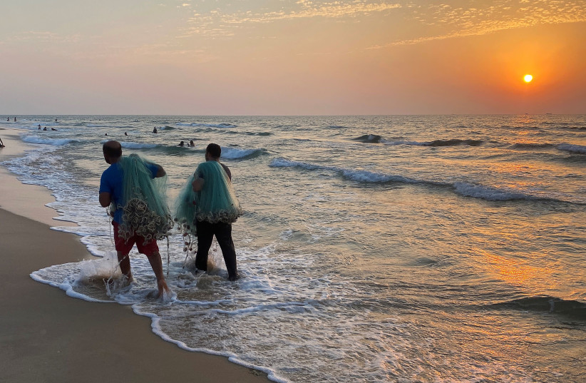 Palestinian fishermen hold their nets as they walk along a beach during a lockdown amid the coronavirus disease (COVID-19) outbreak, in the northern Gaza Strip September 10, 2020 (photo credit: REUTERS/MOHAMMED SALEM)