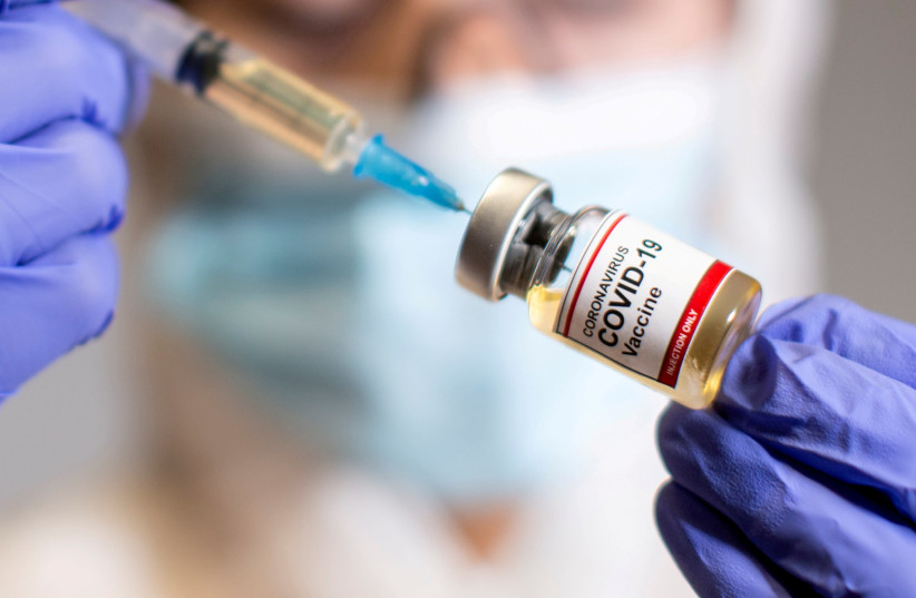 A woman holds a small bottle labeled with a "Coronavirus COVID-19 Vaccine" sticker and a medical syringe, October 30, 2020. (photo credit: REUTERS/DADO RUVIC/FILE PHOTO)
