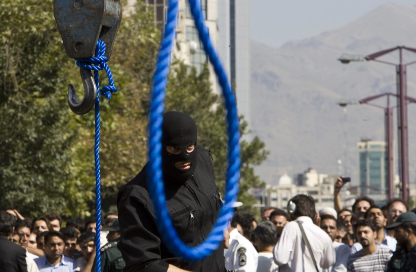 An Iranian policeman takes out his gun ahead of a hanging. (photo credit: REUTERS/RAHEB HOMAVANDI)