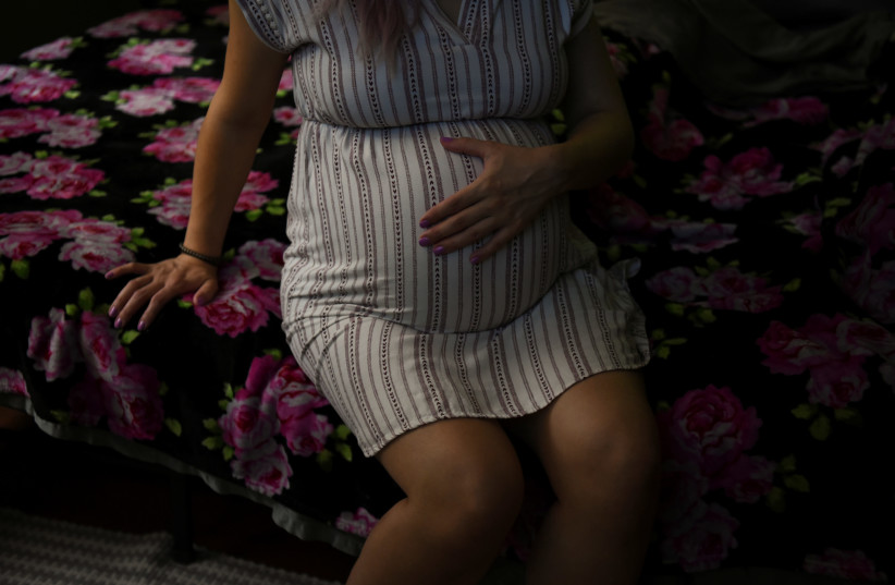 A pregnant woman sits on a bed holding her belly. (photo credit: CALLAGHAN O'HARE/REUTERS)