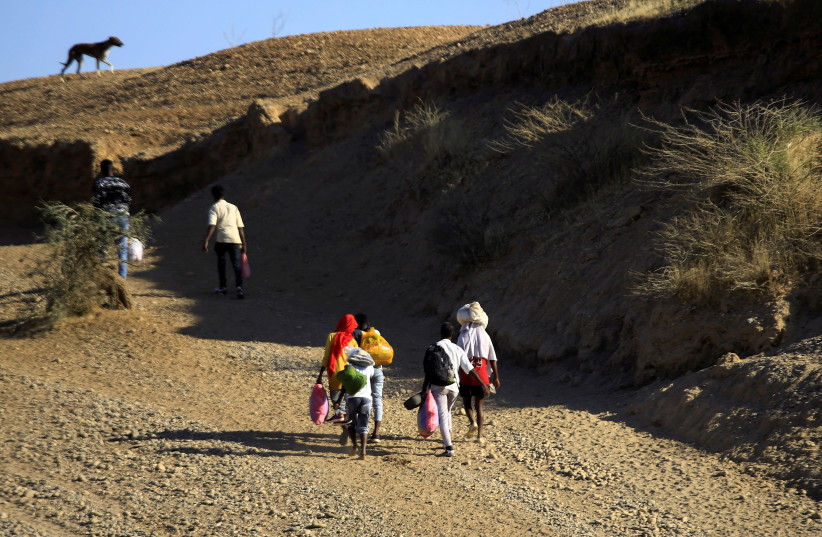 Ethiopians, who fled the ongoing fighting in Tigray region, carry their belongings after crossing the Setit River on the Sudan-Ethiopia border, in the eastern Kassala state, Sudan December 16, 2020. (photo credit: MOHAMED NURELDIN ABDALLAH/REUTERS)