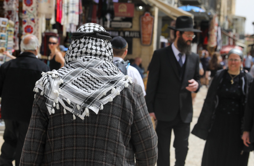 A Palestinian man and an Israeli Ultra-Orthodox Jew are seen walking in Jerusalem's Old City on April 17, 2022 (photo credit: MARC ISRAEL SELLEM/THE JERUSALEM POST)