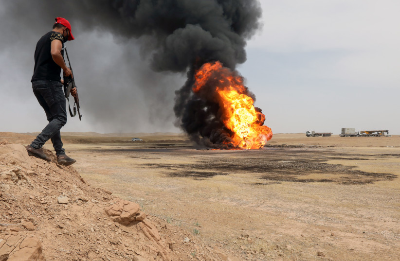 A security member walks as flames and smoke rising from oil wells are seen in the distance at the Bai Hassan oilfield, which was attacked by militants, close to the northern Iraqi city of Kirkuk, Iraq, May 5, 2021. (photo credit: REUTERS/AKO RASHEED)
