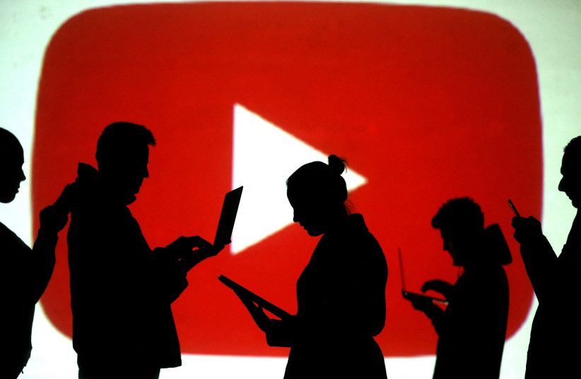   Silhouettes of laptop and mobile device users are seen next to a screen projection of the YouTube logo in this picture illustration taken March 28, 2018.  (photo credit: REUTERS/DADO RUVIC/ILLUSTRATION/FILE PHOTO)