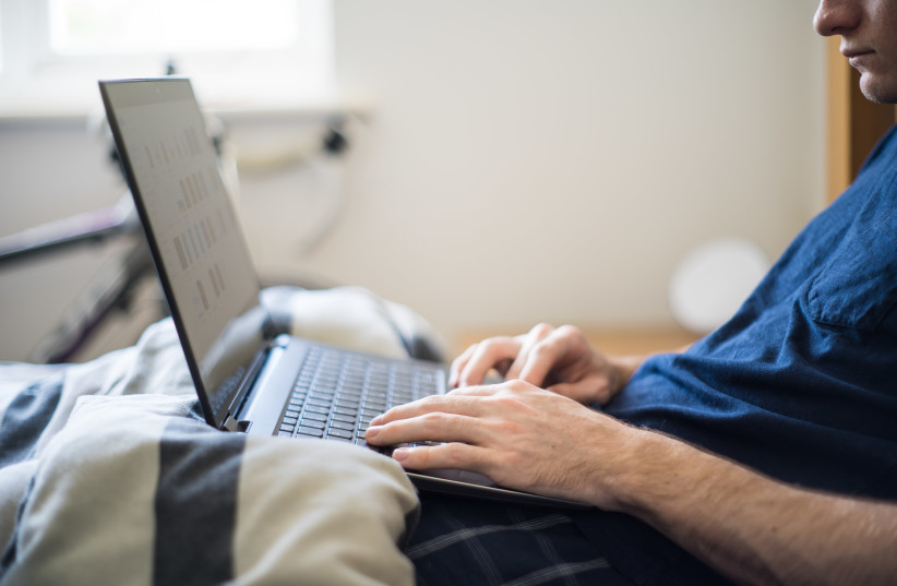  A man working from home works on his laptop from bed. (photo credit: MICRO BIZ MAG/WIKIMEDIA COMMONS)