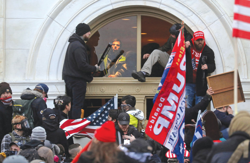  A MOB of supporters of then-US president Donald Trump climb through a window they broke, as they storm the United States Capitol Building in Washington, on January 6, 2021 (photo credit: LEAH MILLIS/REUTERS)