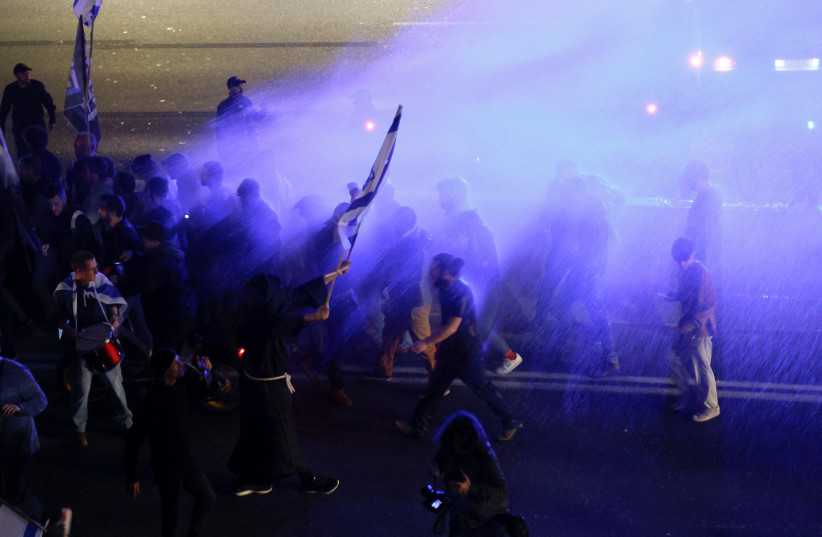 People are sprayed with a water cannon as they block a road during a demonstration, as Israeli Prime Minister Benjamin Netanyahu's government presses on with its contentious judicial overhaul, in Tel Aviv, Israel March 4, 2023. (photo credit: AMIR COHEN/REUTERS)