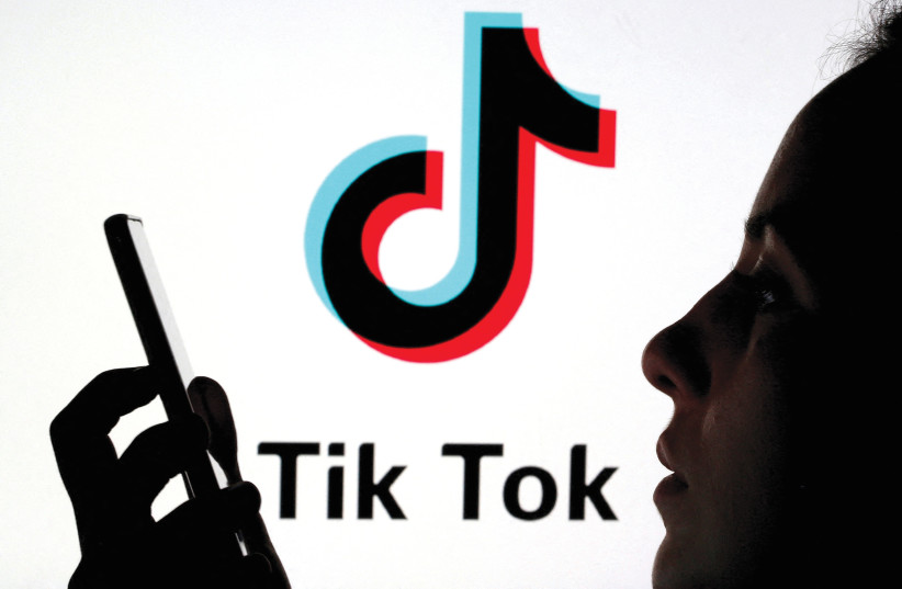  A woman holds a smartphone as a TikTok logo is displayed behind in this picture illustration.  (photo credit: DADO RUVIC/REUTERS)