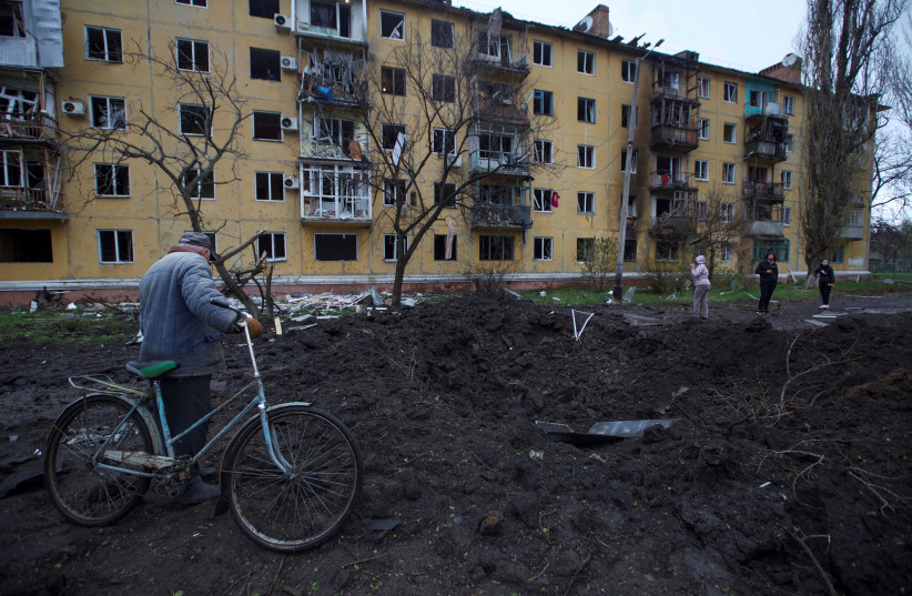 Local residents stand next to a crater left by a Russian missile strike, amid Russia's attack on Ukraine, in Sloviansk, Donetsk region, Ukraine April 14, 2023. (photo credit: Anna Kudriavtseva/Reuters)
