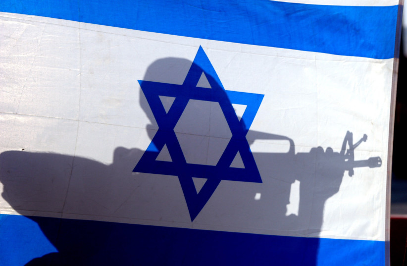  An IDF soldier holding a gun is silhouetted on the national flag. (photo credit: MARC ISRAEL SELLEM/THE JERUSALEM POST)