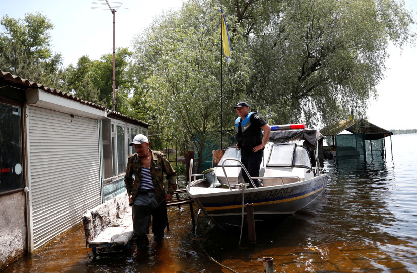 Mykola stands next to a police boat on a flooded island, which locals and officials say is caused by Russia's chaotic control of the Kakhovka dam downstream, amid Russia's attack on Ukraine, near Zaporizhzhia, Ukraine, May 20, 2023. (photo credit: BERNADETT SZABO / REUTERS)