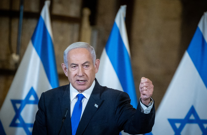 Israeli Prime Minister Benjamin Netanyahu, standing in front of Israeli flags, leads the weekly government conference, held at the Western Wall tunnels in Jerusalem's Old City on May 21, 2023. (photo credit: YONATAN SINDEL/FLASH90)