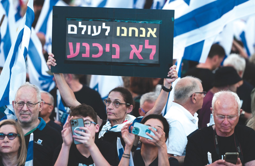  A DEMONSTRATOR holds a sign which reads ‘We will never surrender,’ at a protest against the government’s planned judicial overhaul, in Tel Aviv, last Saturday night.  (photo credit: AVSHALOM SASSONI/FLASH90)