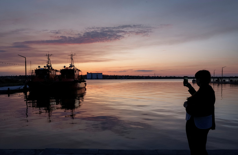  A woman takes a picture of the sunset from an embankment in Mykolaiv, Ukraine, where flood waters from Kakhovka dam destruction reach the city, amid Russia's attack on Ukraine, June 8, 2023. (photo credit: REUTERS/Alina Smutko)