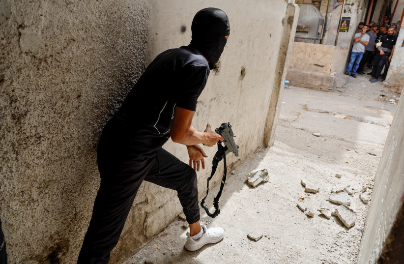  A Palestinian holding a weapon takes cover between buildings amid clashes with Israeli troops during an Israeli raid in Nablus in the West Bank June 13, 2023. (photo credit: RANEEN SAWAFTA/REUTERS)