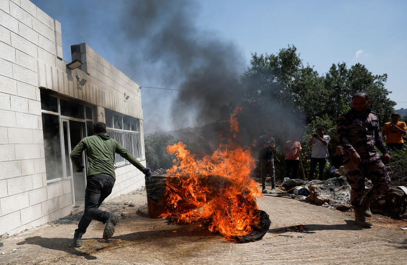  A Palestinian man runs near a burning object, after an attack by Israeli settlers, near Ramallah, in the West Bank, June 21, 2023 (photo credit: REUTERS/MOHAMAD TOROKMAN)