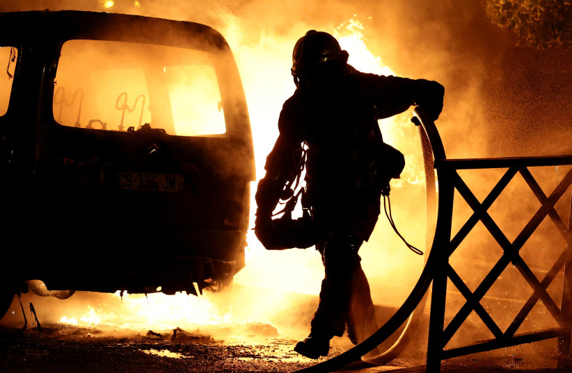  A firefighter works to extinguish burning vehicles during clashes between protesters and police, after the death of Nahel, a 17-year-old teenager killed by a French police officer during a traffic stop, in Nanterre, Paris suburb, France, June 28, 2023 (photo credit: REUTERS/Stephanie Lecocq)