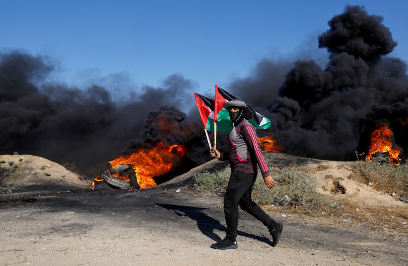  A Palestinian holds flags during a protest against Israeli army raid in Jenin, along Israel-Gaza border fence east of Gaza City July 3, 2023.  (photo credit: MOHAMMED SALEM/REUTERS)