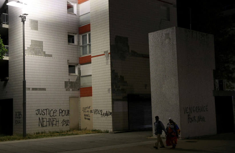 Residents walk past phrases written on walls of buildings at a neighbourhood where Nahel, a 17-year-old teenager, was killed by a French police officer during a traffic stop, in Nanterre, France, July 2, 2023. (photo credit: NACHO DOCE/REUTERS)
