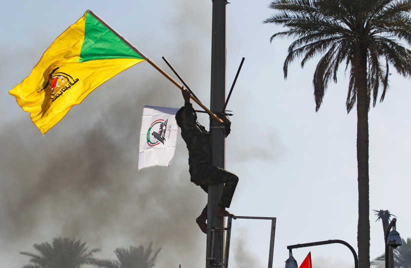 A member of Hashd al-Shaabi (paramilitary forces) holds a flag of Kataib Hezbollah militia group during a protest to condemn air strikes on their bases, in Baghdad, Iraq December 31, 2019 (photo credit: KHALID AL MOUSILY / REUTERS)