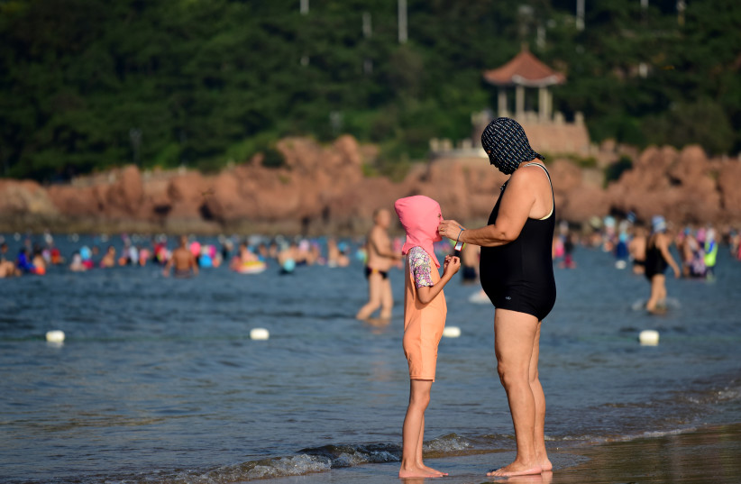  A woman wearing facekini adjusts the mask on a child on a beach on a hot day in Qingdao, Shandong province, China August 10, 2018. Picture taken August 10, 2018 (photo credit: REUTERS/STRINGER)