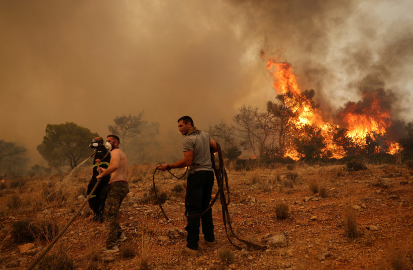  Men help a firefighter as they try to extinguish a wildfire burning near the village Vlyhada, near Athens, Greece, July 19, 2023. (photo credit: REUTERS/STELIOS MISINAS)