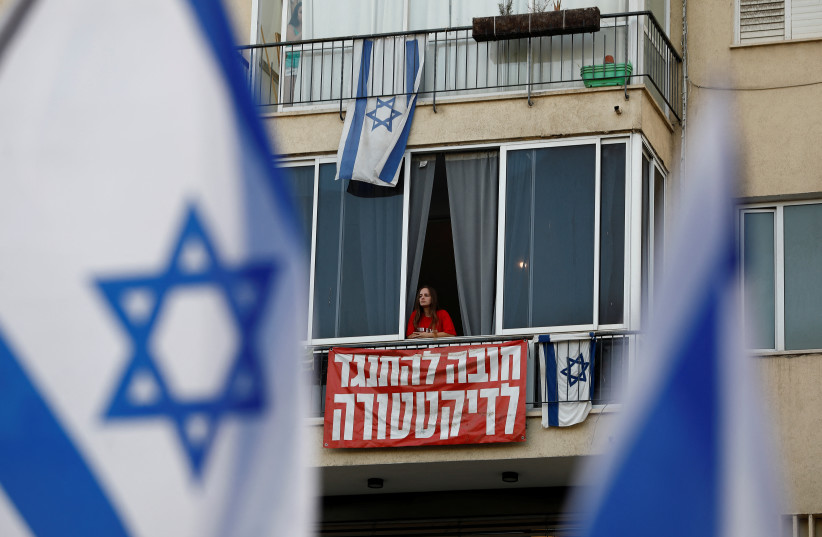  A person looks out, above a banner that reads 'in it to oppose the dictatorship', as people take part in a demonstration against Israeli Prime Minister Benjamin Netanyahu and his nationalist coalition government's judicial overhaul, in Tel Aviv, Israel, July 22, 2023. (photo credit: CORINNA KERN/REUTERS)