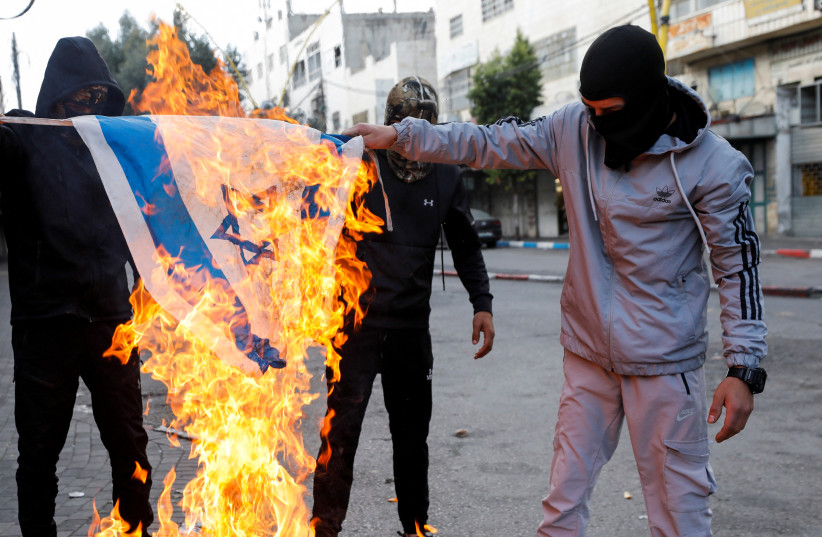  Palestinians burn Israeli flag during clashes with Israeli troops in Hebron, November 18, 2022. (photo credit: REUTERS/MUSSA QAWASMA)