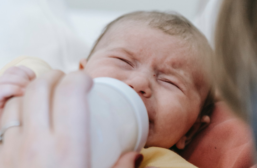 A baby crying while drinking from a bottle. (Illustrative) (photo credit: PEXELS)