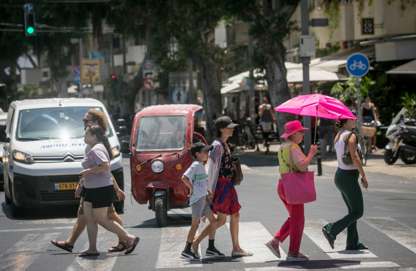  A woman carrying an umbrella to protect her from the sun crosses a street  in Tel Aviv. August 9, 2023. (photo credit: MIRIAM ALSTER/FLASH90)