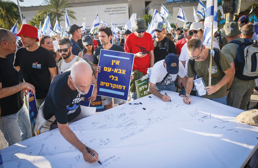  RESERVISTS SIGN a statement that they will not continue serving, as part of the protest against the judicial overhaul, in Tel Aviv, last month. The blue placard reads: ‘There cannot be a people’s army without democracy.’  (photo credit: CHAIM GOLDBEG/FLASH90)