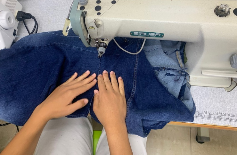  MARYAM STITCHES finishing touches onto her denim ‘Neanderthal dress.’ The women often design according to themes, the most recent of which was denim. (photo credit: ARIEL SHEINBERG)