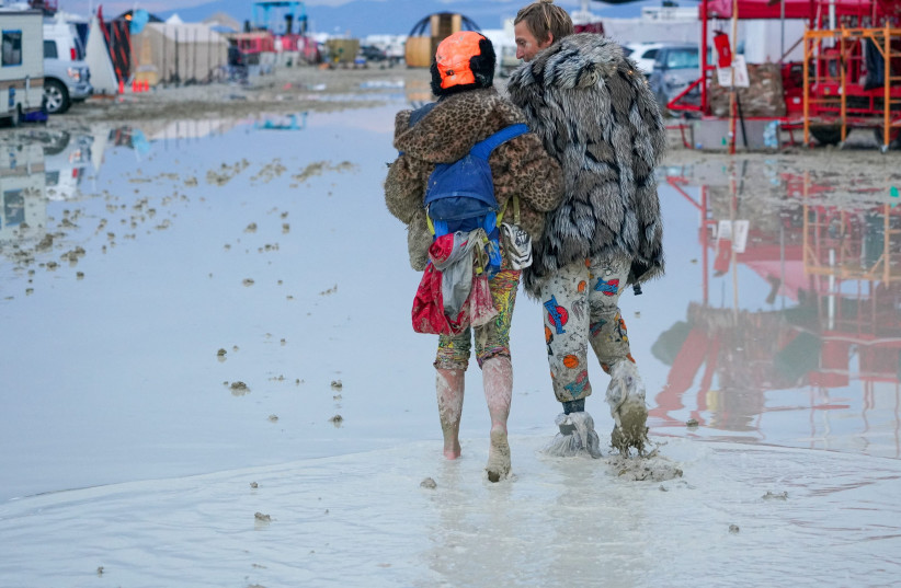  Dub Kitty and Ben Joos, of Idaho and Nevada, walk through the mud at Burning Man after a night of dancing with friends in Black Rock City, in the Nevada desert, after a rainstorm turned the site into mud September 2, 2023.  (photo credit: Trevor Hughes/USA TODAY NETWORK via REUTERS )