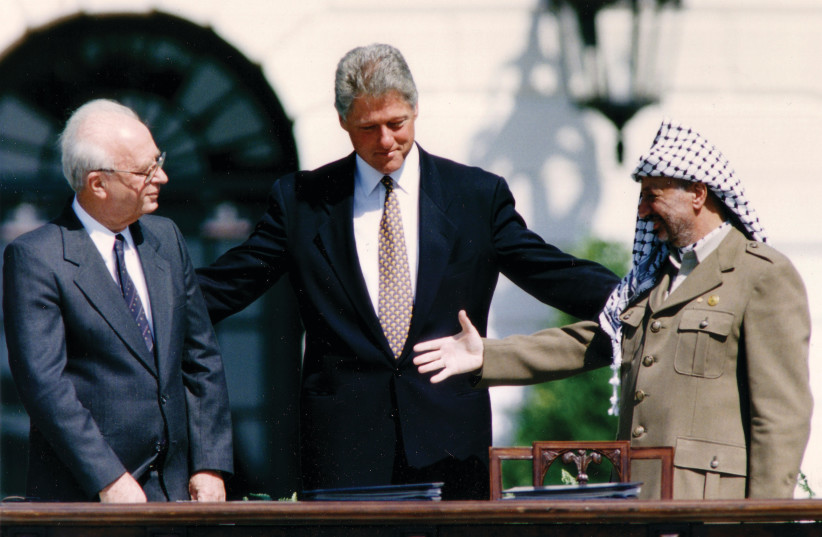  PLO CHAIRMAN Yasser Arafat reaches to shake hands with prime minister Yitzhak Rabin, as US president Bill Clinton encourages them, after the signing of the Declaration of Principles, at the White House, September 13, 1993. (photo credit: GARY HERSHORN/REUTERS)