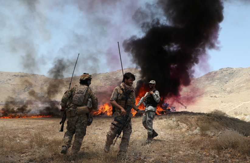  Afghan police officers chat with each others in front of a pile of burning illegal drugs in the outskirts of Kabul, Afghanistan July 1, 2021. (photo credit: REUTERS/OMAR SOBHANI)
