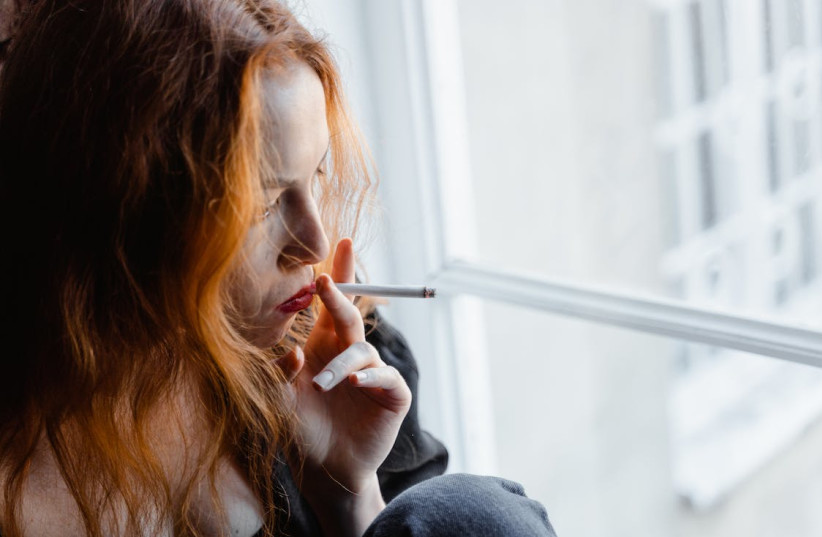 A woman smoking while looking out the window. (photo credit: PEXELS)