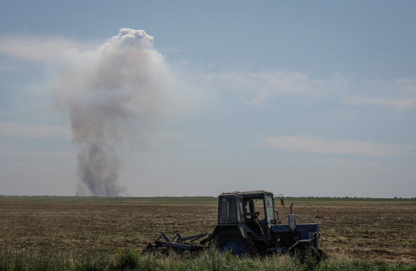 An agricultural worker operates a tractor as smoke rises in the distance after a military strike, amid Russia's attack on Ukraine, in Kherson region, Ukraine June 20, 2023. (photo credit: REUTERS/Andrii Dubchak)