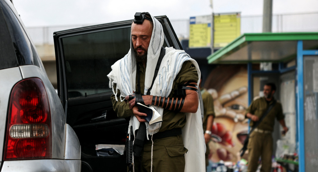 Израильский солдат носит еврейский молитвенный платок и тфилин во время молитвы в Ашкелоне, на юге Израиля, 10 октября 2023 года. (Фото: REUTERS/VIOLETA SANTOS MOURA)
