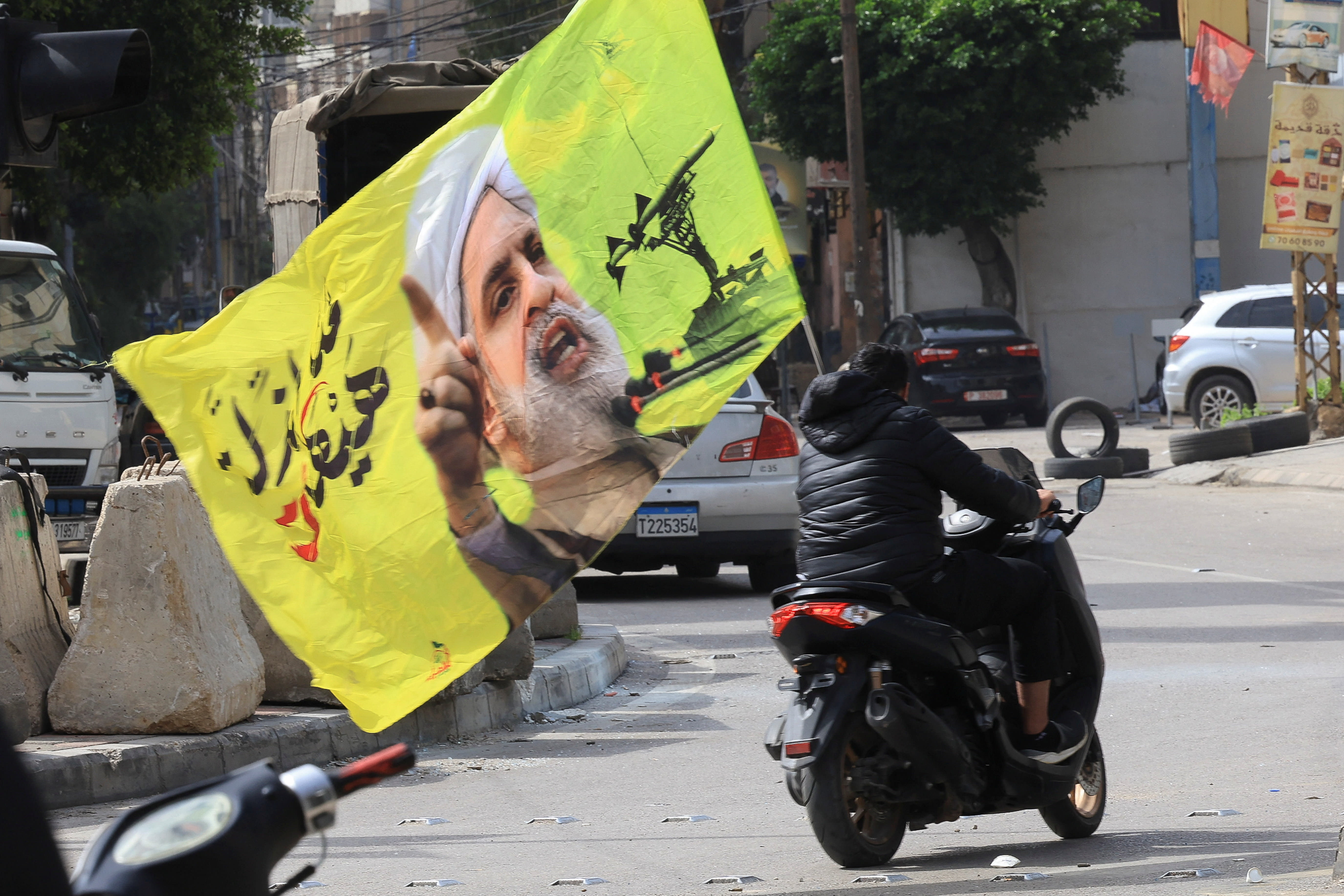A person riding a scooter carries a flag with an image depicting Hezbollah leader Naim Qassem, as displaced people make their way to return to their homes after a 10-day ceasefire between Lebanon and Israel went into effect, at the southern suburbs of Beirut, Lebanon.