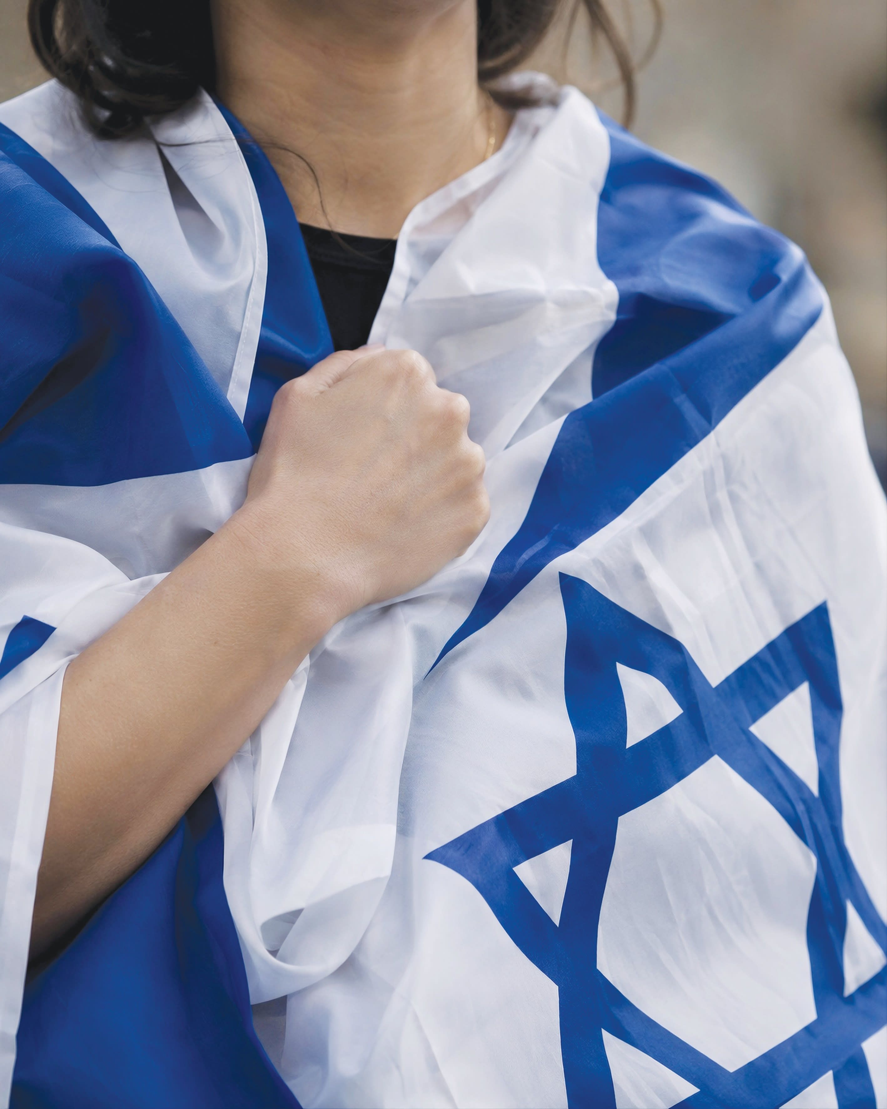 An individual clothed in an Israeli flag recites the Yom Kippur vidui prayer, beating their chest.