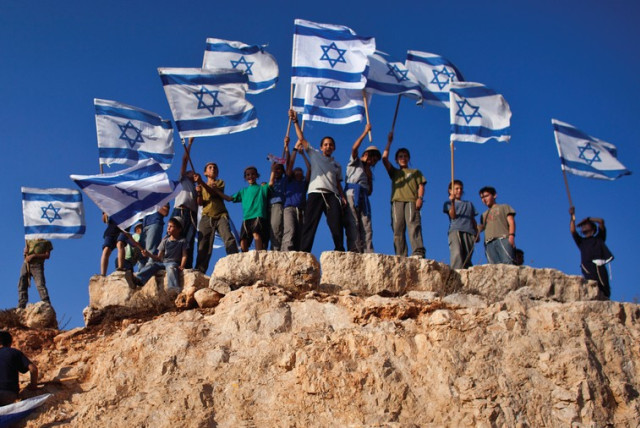 Jewish Youths in Israel wave flags and stand atop a hill. The author recalls his own young days in Zionist youth groups. (credit: REUTERS)