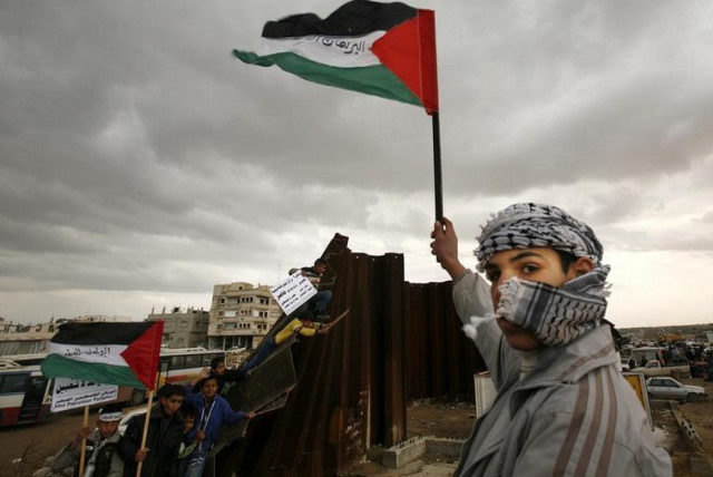 A Palestinian waves a flag near a destroyed section of the border wall between the Gaza Strip and Egypt (photo credit: REUTERS)