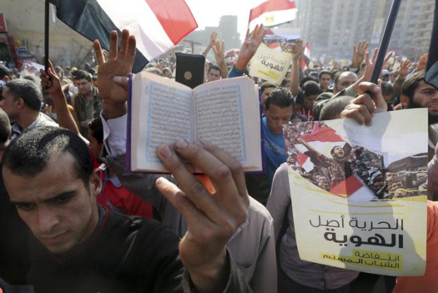 A supporter of the Muslim Brotherhood and ousted Egyptian President Mohamed Mursi holds a copy of the Koran as others shout slogans against the military and the interior ministry during a protest in the Cairo suburb of Matariya November 28, 2014. (credit: MOHAMED ABD EL GHANY/REUTERS)