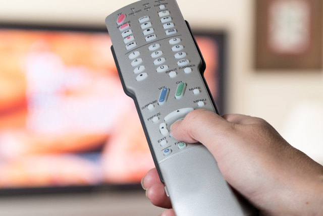 Silver television remote control being pressed by thumb with out of focus screen background (Illustrative) (photo credit: INGIMAGE)