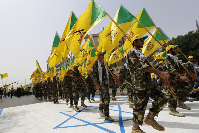 Iraqi Shi'ite Muslim men from the Iranian-backed group Kataib Hezbollah wave the party's flags as they walk along a street painted in the colours of the Israeli flag during a parade marking the annual Quds Day, or Jerusalem Day, on the last Friday of the Muslim holy month of Ramadan, in Baghdad (credit: THAIER AL-SUDANI/REUTERS)