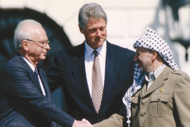 PLO Chairman Yasser Arafat (right) shakes hands with Israeli Prime Minister Yitzhak Rabin (left), as U.S. President Bill Clinton stands between them, after the signing of the Israeli-PLO peace accord, at the White House in Washington, on September 13, 1993 (credit: GARY HERSHORN/REUTERS)